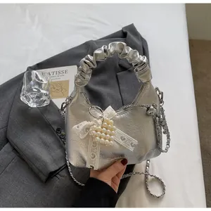 Detail of silver pleated handbag featuring heart pearl and lace bow charm accessories