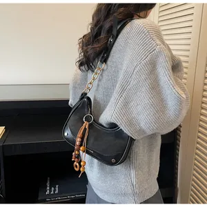 Detail of black hobo bag featuring gold chain strap and decorative wooden bead tassel