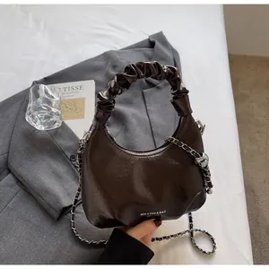 Detail shot of a glossy brown half-moon bag with a scrunchie handle and silver chain strap