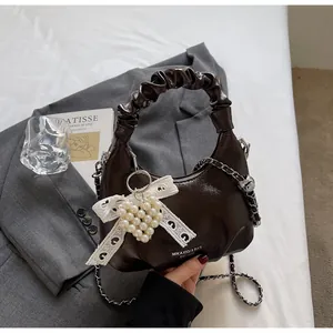 Detail of dark brown glossy bag with pleated handle and white lace bow heart charm
