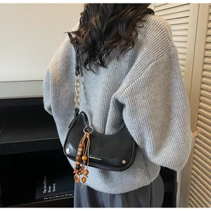 Detail of black leather half-moon bag with metallic studs and beaded tassel charm on model