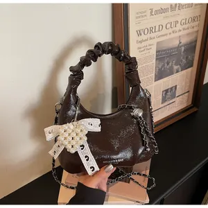 Close-up of a brown patent leather bag with pleated handle and pearl heart charm decoration