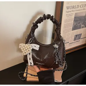 Detail of a shiny brown patent leather mini bag with pleated handle and metallic chain