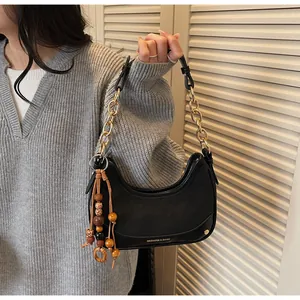 Detail of black leather hobo bag with gold chain strap and colorful bead tassel accessory