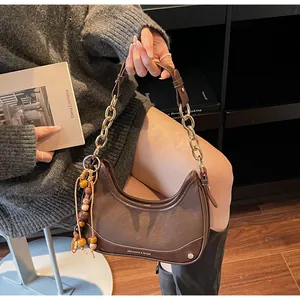 Detail of a dark brown half-moon bag with gold chain strap and bohemian fringe charm
