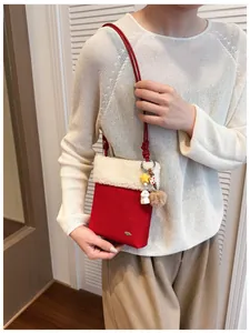 Détail d'un sac bandoulière rouge avec bord en peluche blanche et breloques de fête