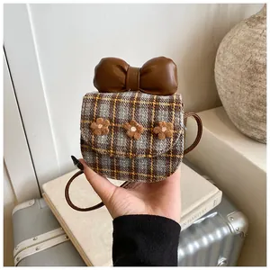 Detail of mini plaid crossbody bag with large brown bow and floral accents on tweed