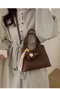 Detail of dark brown leather bucket bag with metal turn-lock and teddy bear charm accessory