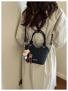 Detail of black leather bucket bag featuring a tubular handle and a plush bear pendant