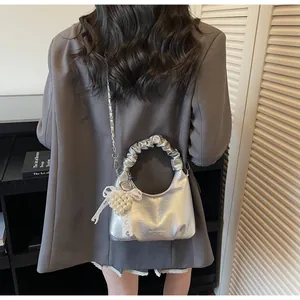 Detail of silver metallic Boston handbag featuring ruched handles and a pearl heart charm