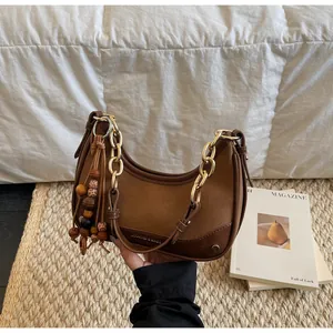 Detail of a brown half-moon bag with gold chain strap and vintage wooden bead charm