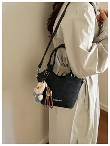 Detail of black matte leather bucket bag with bear charm and long shoulder strap