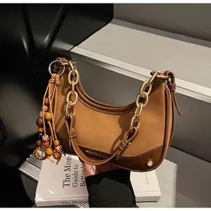 Detail of a brown leather patchwork shoulder bag with gold chain and wooden bead tassel