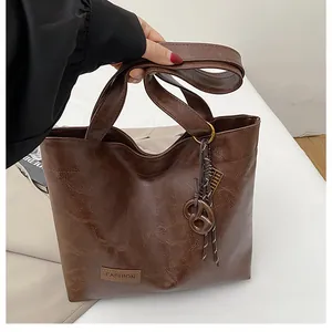 Détail du cabas marron foncé avec texture grainée, étiquette en cuir et ornement tressé
