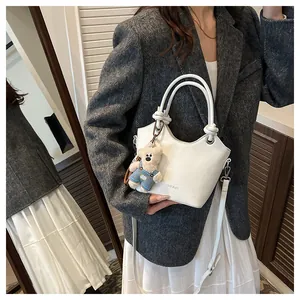 Detailed view of white leather bucket bag with top handles and cute bear charm accessory