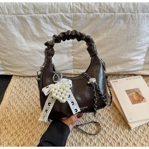 Detail of dark brown patent leather mini bag with pleated handle and pearl heart charm