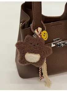 Close-up of a brown plush bear charm with woven ropes on a lychee grain leather handbag