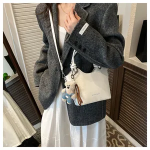 Detail of white faux leather bucket bag with gold logo and blue denim teddy bear charm