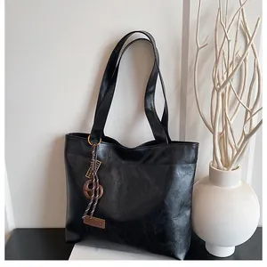 Détail du sac cabas noir avec texture froissée mate, breloque tressée et étiquette