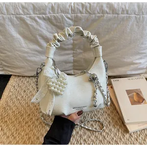 Close-up of white leather hobo bag with pleated handle and pearl heart charm detail