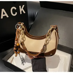 Detail of hobo bag with gold logo, chain strap, and decorative tassel in luxury gift box