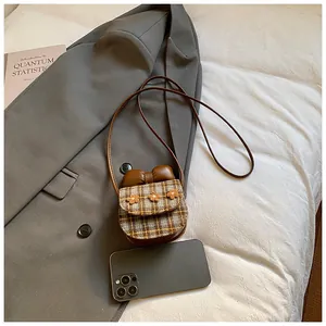 Mini checkered tweed bag with leather bow and floral details shown next to a smartphone