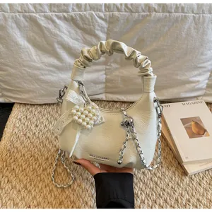 Detail of a creamy white pleated hobo bag with heart pearl charm and logo branding