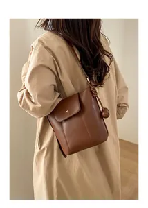 Detail of a dark brown oiled leather bucket bag featuring a decorative round ball charm