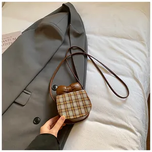Close-up of mini checkered crossbody bag with decorative bow and premium brown leather texture
