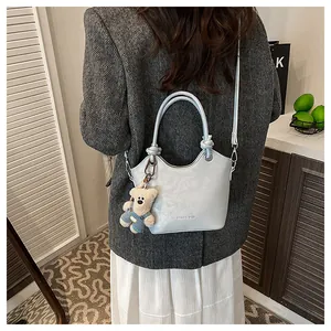 Detail of light blue bucket bag with plush bear charm and crossbody strap on model