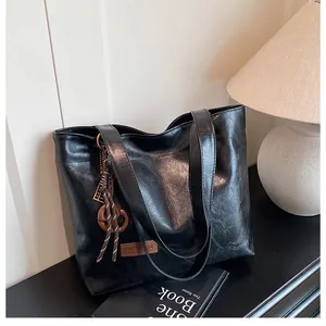 Détail macro du sac cabas noir avec empiècement en cuir marron et breloque à franges