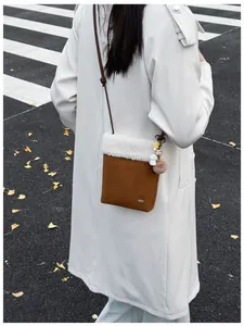 Détail du sac à bandoulière en daim marron avec bordure en peluche blanche et pendentif