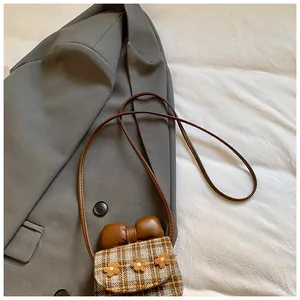 Close-up of a plaid mini crossbody bag with bow and floral details on a grey blazer