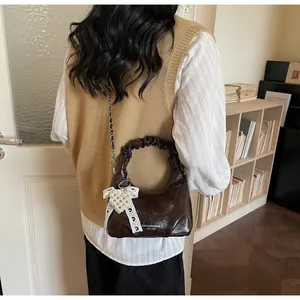 Close-up of brown patent leather mini bag with pleated handle and pearl heart charm