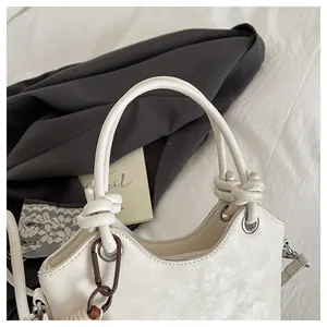 Detail of white bucket bag with knot handle, metallic eyelets, and textured leather finish