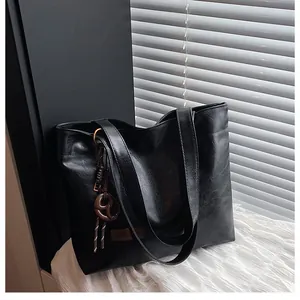 Détail d'un cabas noir en cuir texturé avec de longues anses et un charme marron