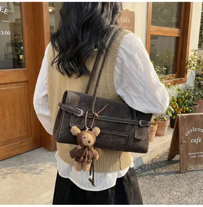 Detail of dark brown faux suede shoulder bag with bear pendant and decorative metal buckles