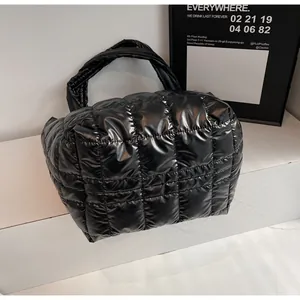 Dettaglio borsa shopper nera lucida trapuntata con manici larghi su podio bianco