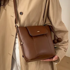 Brown oil wax leather bucket bag with drawstring pompom details and adjustable strap