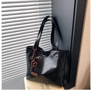Détail du grand sac cabas noir brillant avec étiquette de mode et pendentif marron