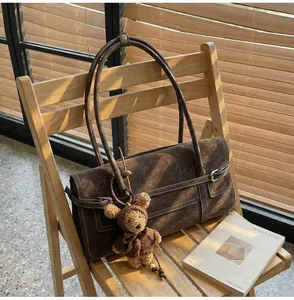 Detailed side view of brown suede shoulder bag with white stitching and teddy bear charm