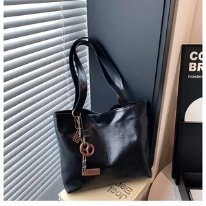 Détail d'un sac cabas en cuir noir brillant avec longues lanières et charm en forme de cœur