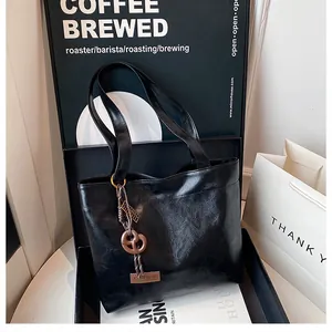Détail du sac cabas en cuir ciré noir brillant avec pendentif décoratif tendance