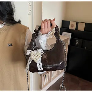 Detail of dark brown patent leather crossbody bag with lace bow and pearl heart charm