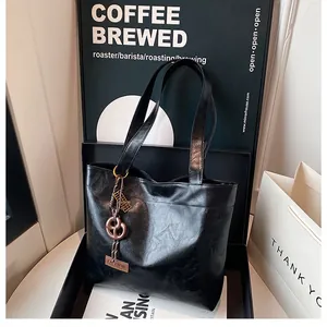 Détail du sac cabas noir brillant avec double bandoulière et pendentif métallique