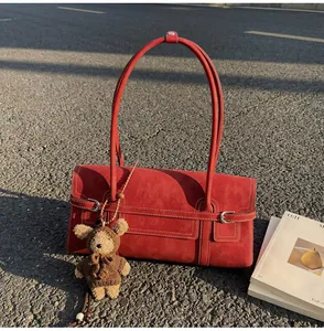 Detail of red leather shoulder bag with bear charm on outdoor asphalt background