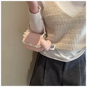 Détail du sac selle rose à pois rouges avec bordure en dentelle et breloque en cœur