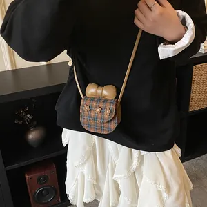 Mini plaid crossbody bag with brown leather bow and floral accents in a vintage setting