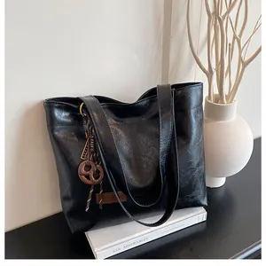Détail du cabas texturé noir avec pendentif à nœud marron et étiquette en cuir gaufré