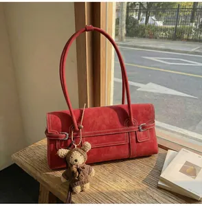 Close-up of deep red suede shoulder bag with silver buckle and cute teddy bear charm